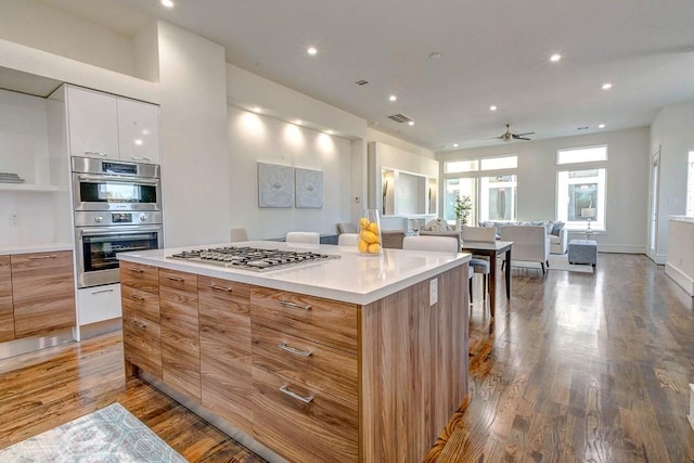 kitchen featuring a kitchen island, hardwood / wood-style floors, white cabinets, ceiling fan, and stainless steel appliances