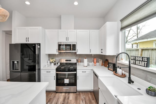 kitchen with light hardwood / wood-style flooring, appliances with stainless steel finishes, sink, backsplash, and white cabinets