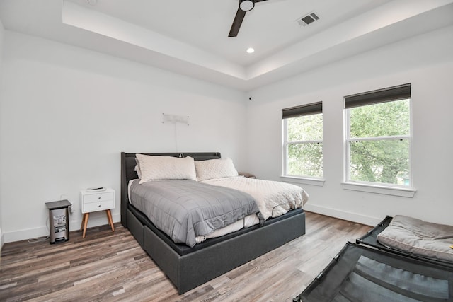 bedroom with ceiling fan, hardwood / wood-style floors, and a tray ceiling