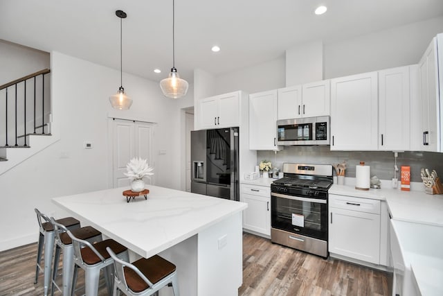 kitchen featuring appliances with stainless steel finishes, a kitchen island, a kitchen bar, decorative light fixtures, and white cabinetry