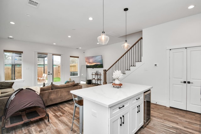 kitchen featuring a kitchen bar, hanging light fixtures, white cabinets, a kitchen island, and beverage cooler