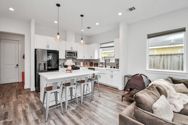 kitchen featuring white cabinets, stainless steel appliances, a center island, and hanging light fixtures