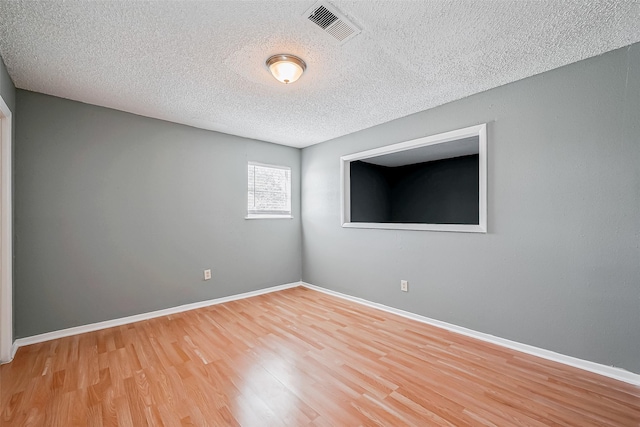 empty room with a textured ceiling and light hardwood / wood-style flooring