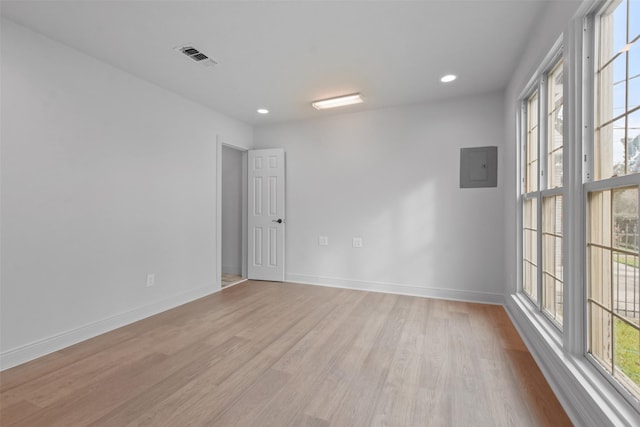 empty room with light wood-type flooring, electric panel, and a healthy amount of sunlight