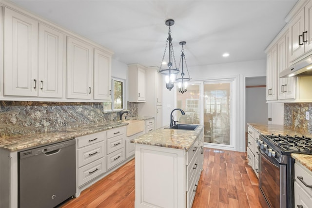 kitchen featuring black dishwasher, tasteful backsplash, a kitchen island with sink, gas range, and pendant lighting