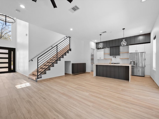 kitchen with ceiling fan, decorative light fixtures, stainless steel fridge with ice dispenser, a center island with sink, and light hardwood / wood-style floors