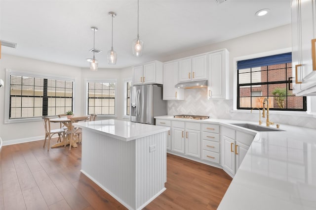 kitchen with white cabinetry, sink, hanging light fixtures, stainless steel fridge, and backsplash