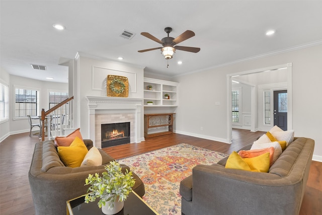 living room featuring crown molding, a tiled fireplace, ceiling fan, and dark hardwood / wood-style flooring