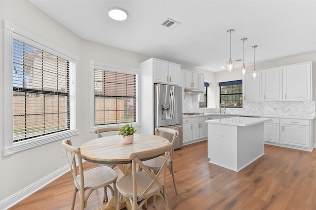 kitchen with white cabinets, stainless steel appliances, a kitchen island, and decorative light fixtures