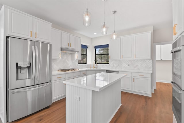 kitchen featuring wood-type flooring, appliances with stainless steel finishes, decorative light fixtures, white cabinetry, and a kitchen island