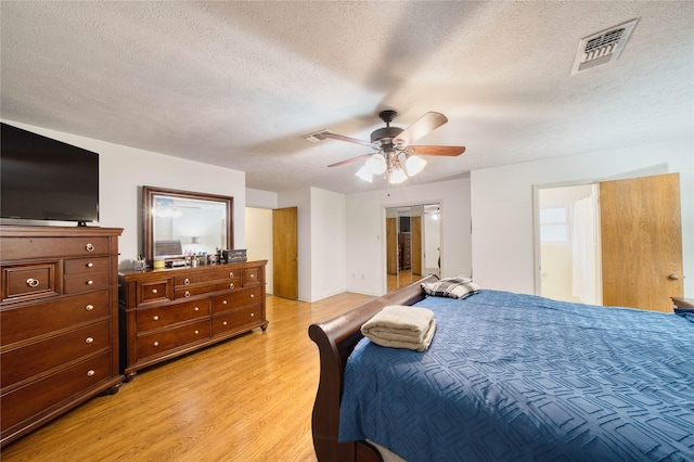 bedroom with ceiling fan, a textured ceiling, light hardwood / wood-style flooring, and ensuite bath