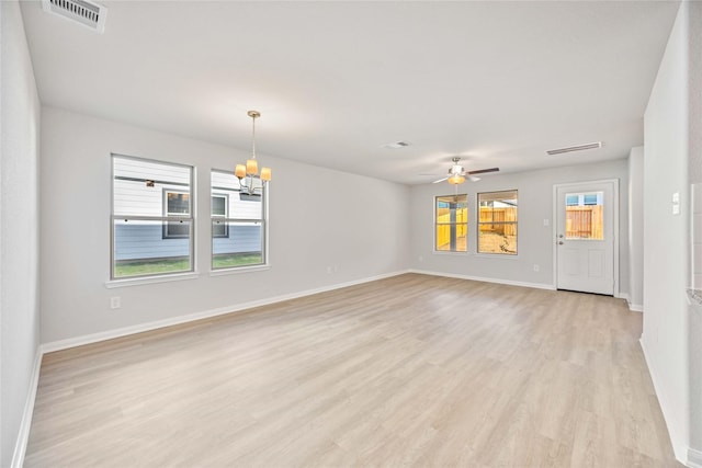 unfurnished living room with ceiling fan with notable chandelier, light hardwood / wood-style floors, and a wealth of natural light