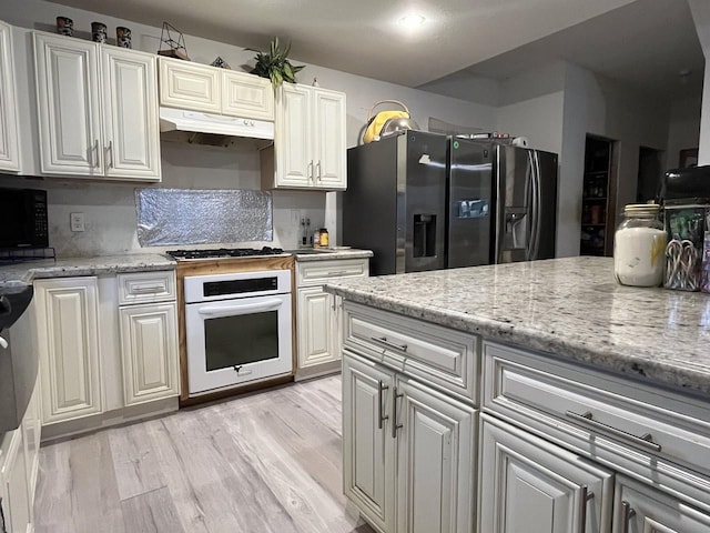 kitchen with white cabinets, light hardwood / wood-style flooring, light stone countertops, and stainless steel appliances