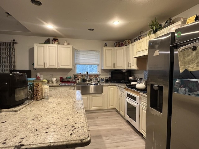 kitchen featuring light hardwood / wood-style flooring, sink, white cabinetry, stainless steel fridge with ice dispenser, and oven