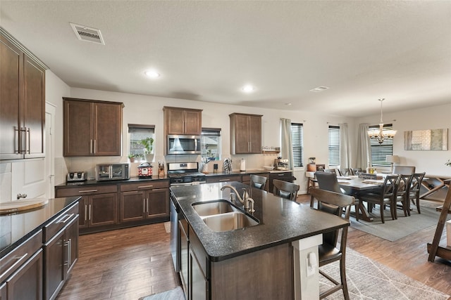 kitchen featuring a kitchen island with sink, sink, pendant lighting, dark wood-type flooring, and stainless steel appliances