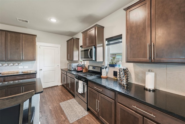 kitchen featuring appliances with stainless steel finishes, dark hardwood / wood-style flooring, dark brown cabinets, and tasteful backsplash