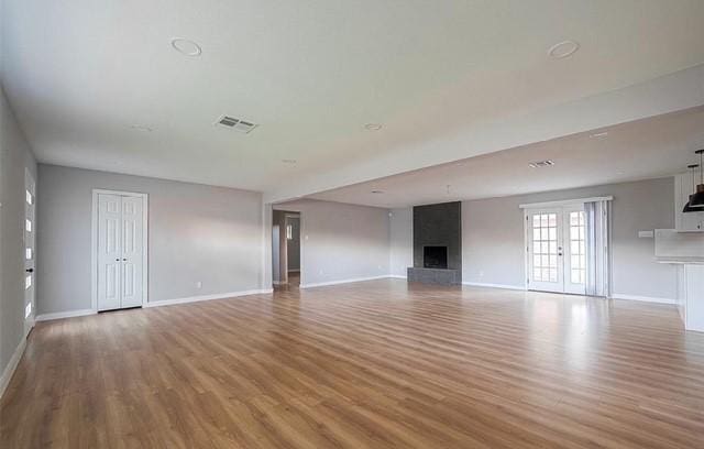 unfurnished living room with hardwood / wood-style flooring, a tile fireplace, and french doors