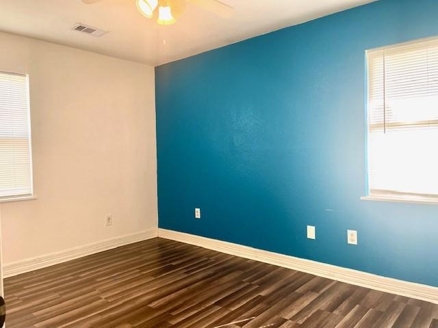 empty room featuring ceiling fan, a healthy amount of sunlight, and dark wood-type flooring