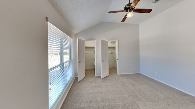 unfurnished bedroom featuring a spacious closet, lofted ceiling, a closet, ceiling fan, and light colored carpet