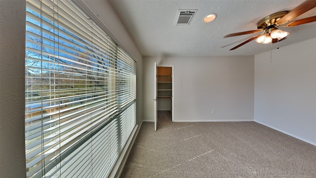 carpeted empty room featuring ceiling fan, plenty of natural light, and a textured ceiling