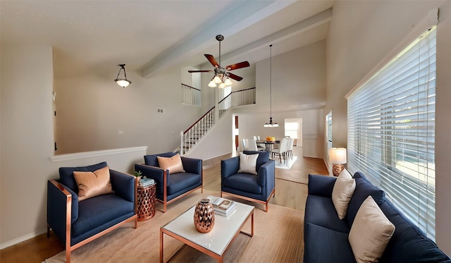 living room featuring beam ceiling, a towering ceiling, ceiling fan, and light wood-type flooring