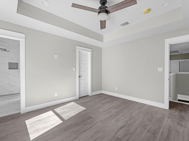 unfurnished bedroom featuring ceiling fan, hardwood / wood-style flooring, a tray ceiling, and ensuite bathroom