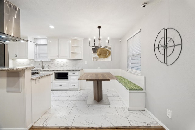 kitchen featuring built in microwave, hanging light fixtures, white cabinetry, light stone counters, and island range hood