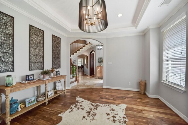 foyer entrance featuring hardwood / wood-style flooring, crown molding, a raised ceiling, and a chandelier