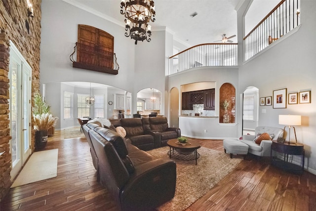 living room featuring hardwood / wood-style flooring, ceiling fan with notable chandelier, a high ceiling, and ornamental molding