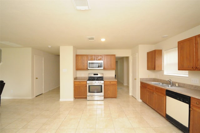 kitchen featuring brown cabinetry, stainless steel appliances, light countertops, and a sink