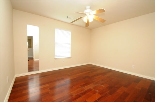 spare room featuring visible vents, ceiling fan, baseboards, and dark wood finished floors