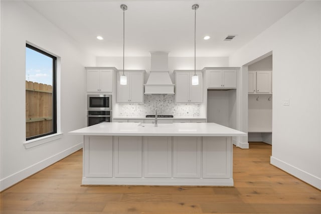 kitchen with built in microwave, an island with sink, custom range hood, and pendant lighting