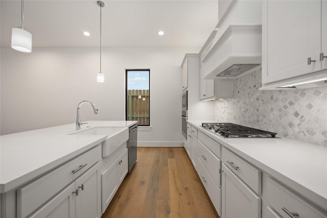 kitchen with sink, white cabinetry, custom range hood, pendant lighting, and stainless steel appliances