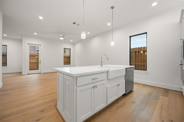 kitchen featuring decorative light fixtures, an island with sink, dishwasher, sink, and white cabinets