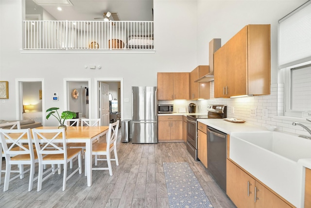 kitchen featuring light wood finished floors, stainless steel appliances, light countertops, a sink, and wall chimney range hood