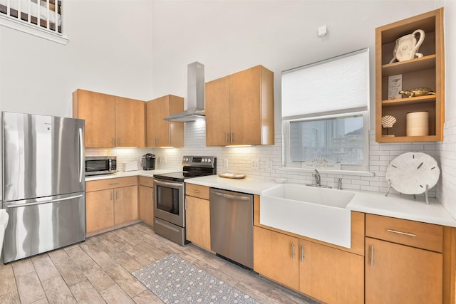 kitchen with decorative backsplash, stainless steel appliances, light countertops, wall chimney range hood, and a sink