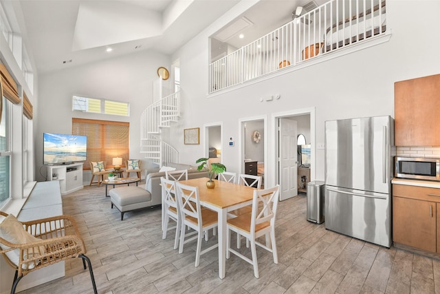 dining area featuring light wood-type flooring, a towering ceiling, stairway, and recessed lighting