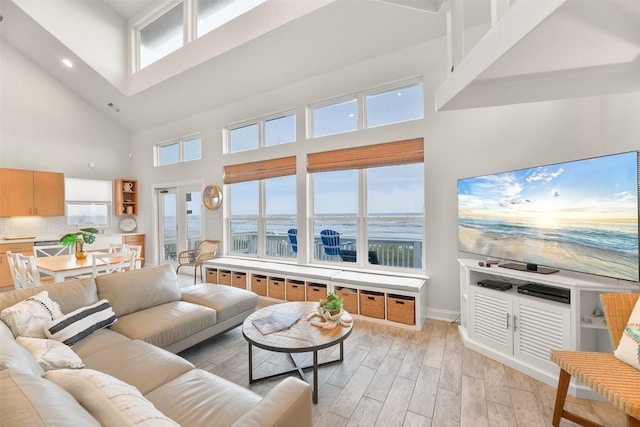 living room featuring light wood-type flooring, a towering ceiling, a wealth of natural light, and baseboards