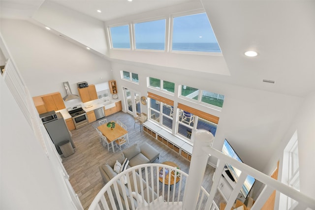 living room with recessed lighting, a high ceiling, a water view, wood finished floors, and visible vents