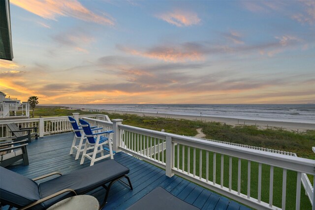 deck at dusk with a water view, a yard, and a beach view