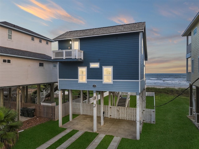 back of property at dusk with a shingled roof, a water view, a balcony, a carport, and stairs