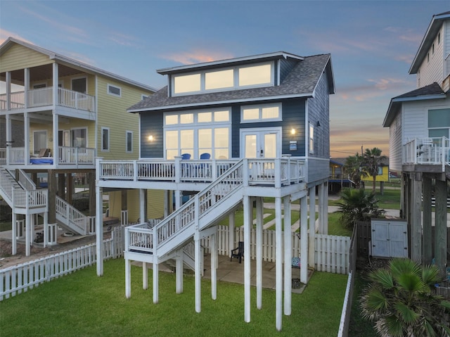 rear view of property with a shingled roof, fence, a lawn, and stairs