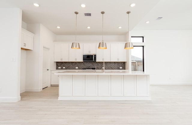kitchen featuring visible vents, white cabinets, backsplash, and stainless steel microwave
