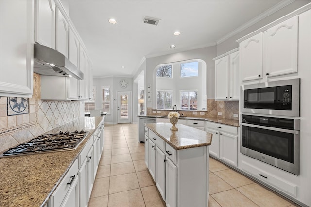 kitchen featuring a kitchen island, stainless steel appliances, sink, light tile patterned flooring, and light stone counters