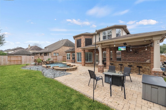 rear view of property with an in ground hot tub, a patio area, a yard, and an outdoor fire pit