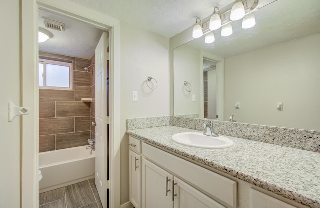 bathroom with tiled shower / bath combo, vanity, and a textured ceiling