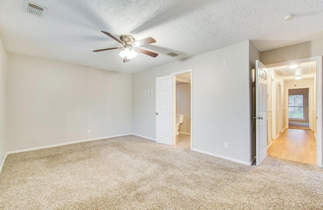 unfurnished bedroom featuring connected bathroom, light carpet, a textured ceiling, and ceiling fan