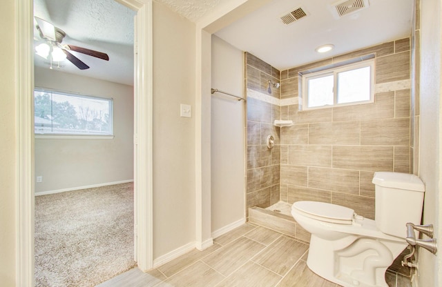 bathroom featuring ceiling fan, a textured ceiling, toilet, and tiled shower