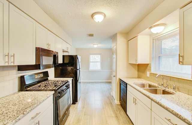 kitchen with sink, tasteful backsplash, light stone counters, black appliances, and white cabinets