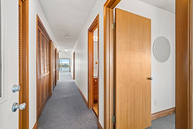 hallway with dark carpet and a textured ceiling